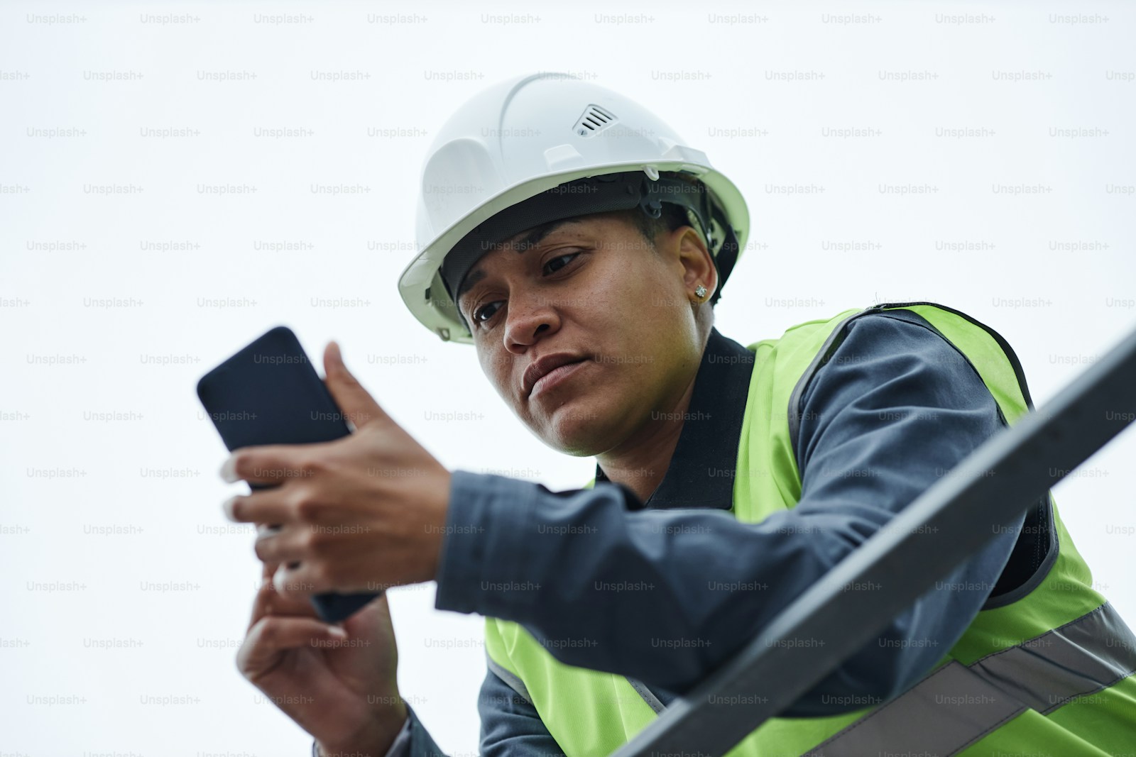 Female construction worker in hard hat holding smartphone against open sky