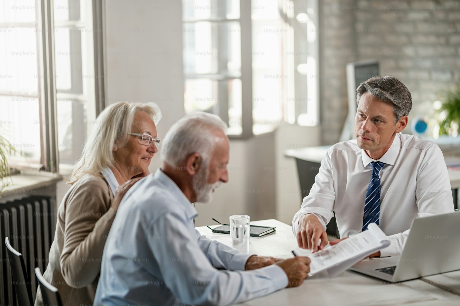 Senior couple signing contract with CPA financial advisor at office table
